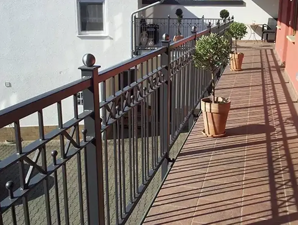 Balkon mit braunem Metallgeländer und mehreren großen Terrakottatöpfen mit kleinen Bäumen