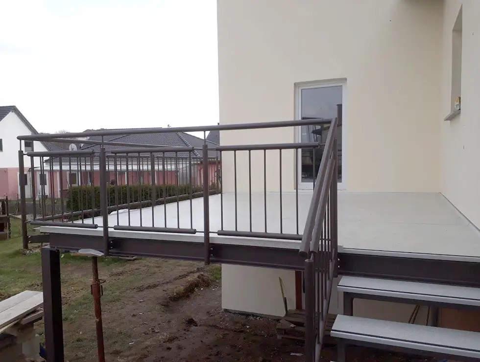 Balkon mit Metallgeländer und zwei Stufen an einem hellen Gebäude