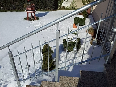 Schneebedeckter Garten mit Treppe und silbernem Metallgeländer im Vordergrund