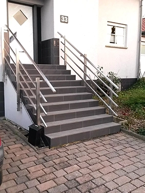 Außentreppe mit grauen Stufen und Edelstahlgeländer an einem weißen Gebäude mit Hausnummer 33