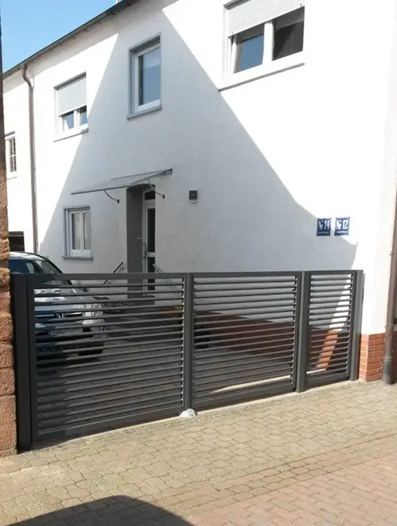 Einfamilienhaus mit weißer Fassade, zwei Fenstern, einer offenen Haustür und einem schwarzen Metallzaun im Vordergrund