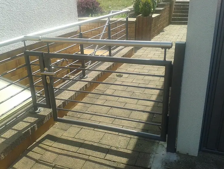 Metallgittertor mit horizontalen Stäben, das an einem Haus befestigt ist und einen gepflasterten Weg absperrt