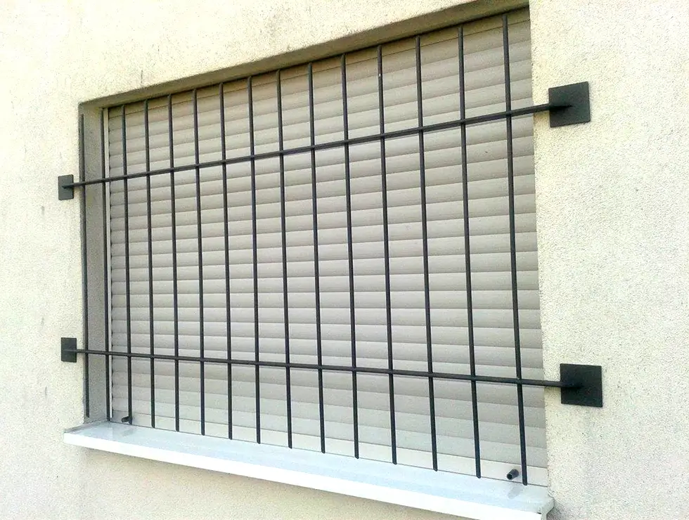 Fenster mit geschlossener Jalousie und schwarzem Gitter vor weißer Wand