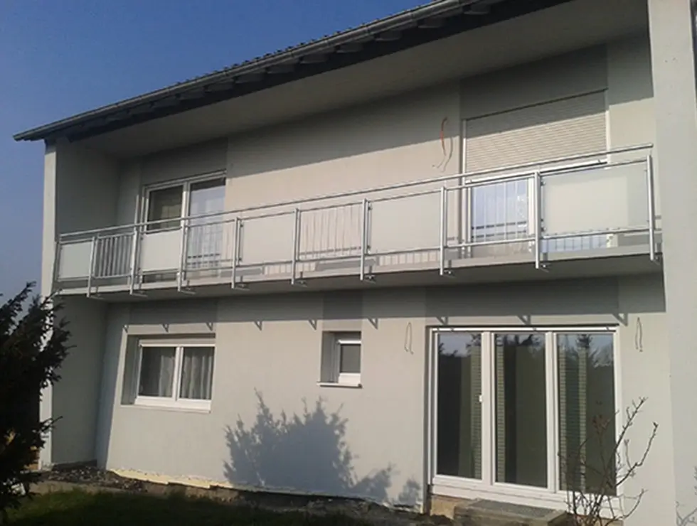 Fassade eines zweistöckigen Hauses mit Balkon und mehreren Fenstern