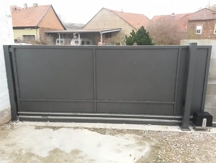 Schwarzes, modernes Schiebetor aus Metall vor einem Hof mit Häusern im Hintergrund