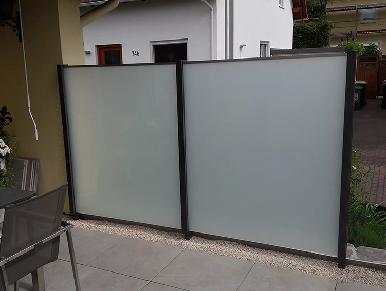 Zwei nebeneinander stehende Sichtschutzwände aus mattiertem Glas mit schwarzem Rahmen auf einer Terrasse