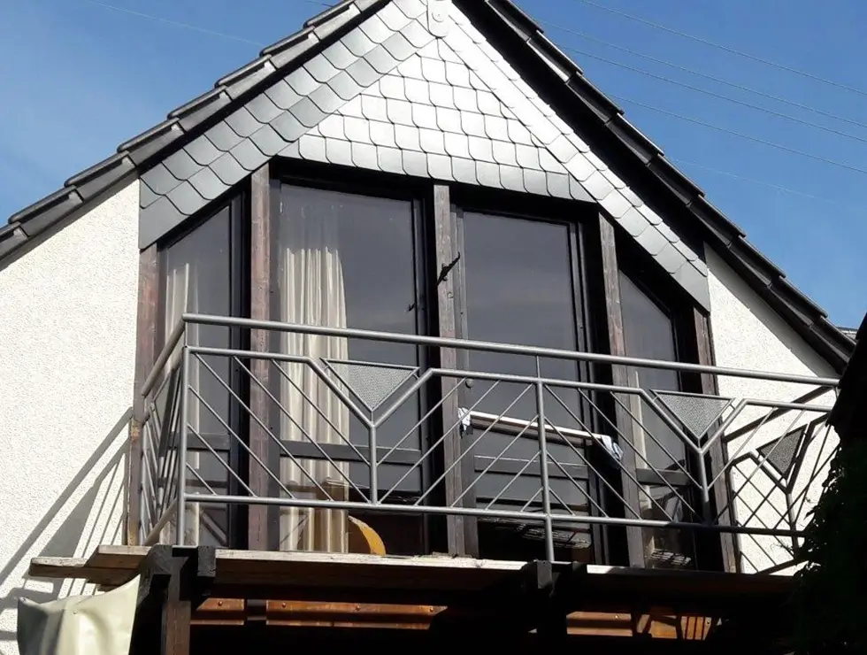 Giebelfenster mit dreieckigem Dach und Balkon mit Metallgeländer an einem weißen Haus
