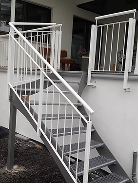 Außentreppe mit weißem Metallgeländer und Gitterroststufen an einem Gebäude