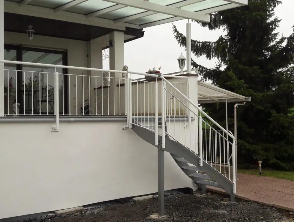 Außentreppe mit Metallgeländer führt zu überdachter Terrasse an einem weißen Haus