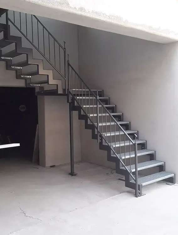 Metalltreppe mit Gitterroststufen und Geländer in einem hellen Raum mit Betonboden
