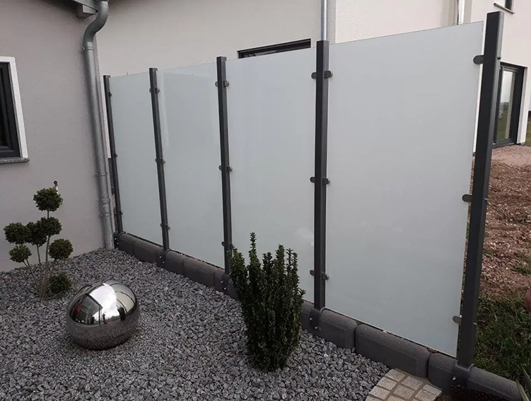 Garten mit grauem Kies, drei blickdichten Sichtschutzwänden aus Milchglas und einer reflektierenden silbernen Kugel