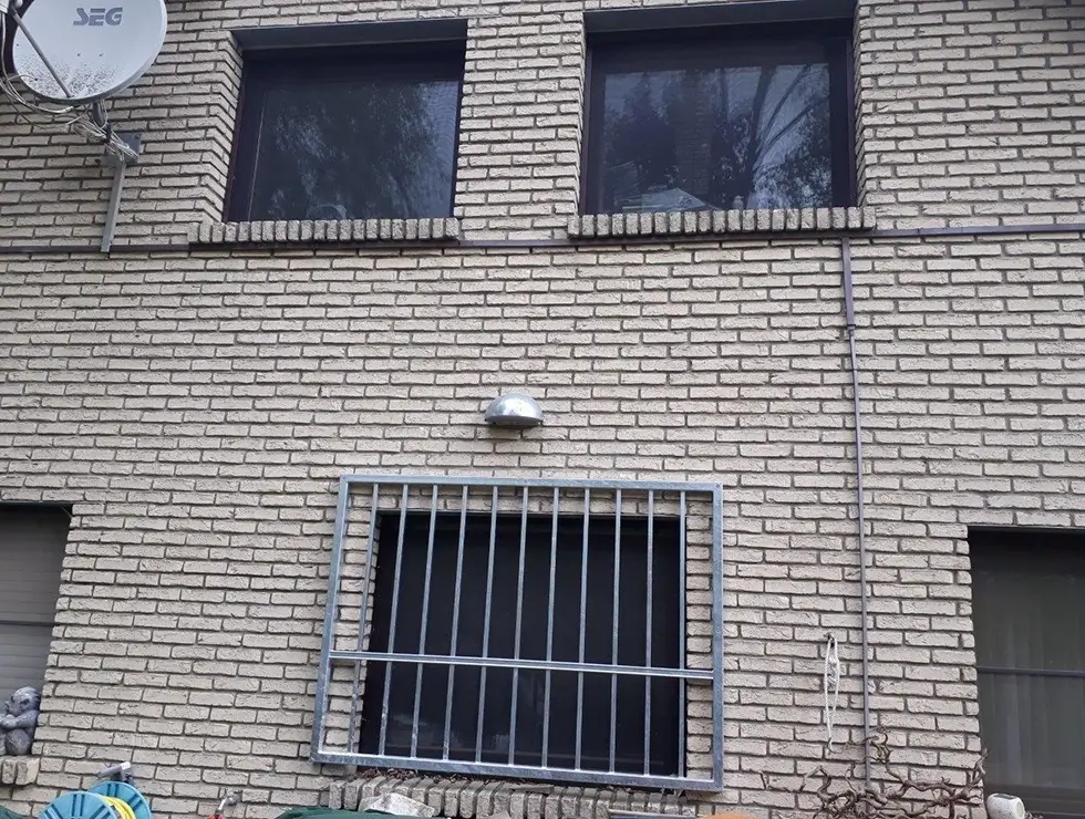 Fassade eines Gebäudes mit zwei Fenstern oben, einem vergitterten Fenster unten und einer Satellitenschüssel links oben