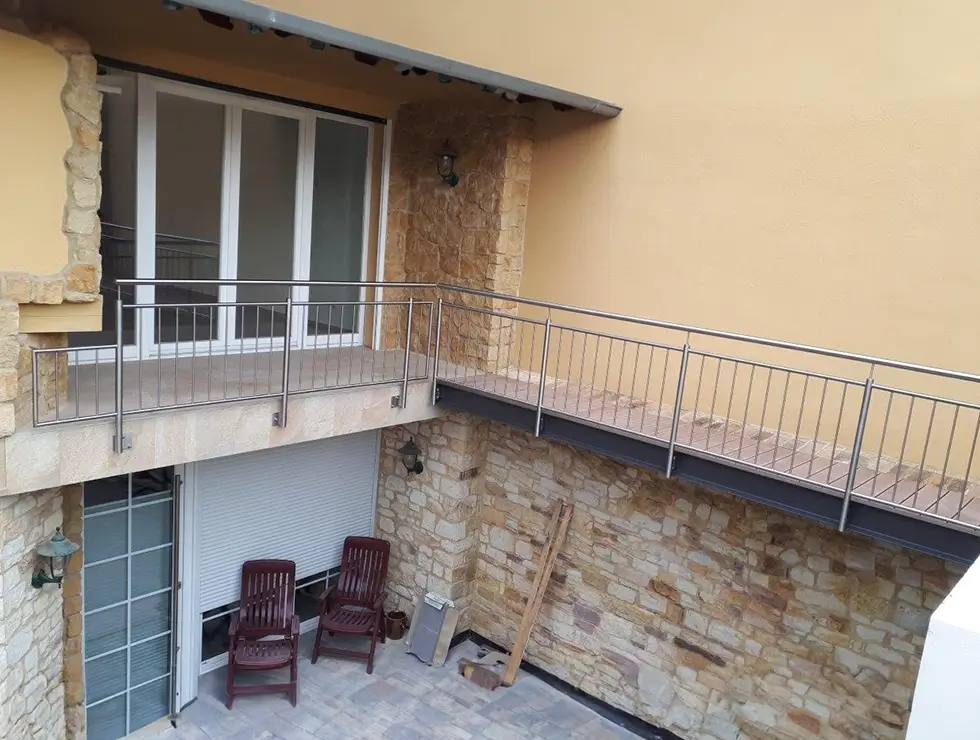 Balkon mit Metallgeländer an einem Haus mit Natursteinfassade und zwei Holzstühlen darunter