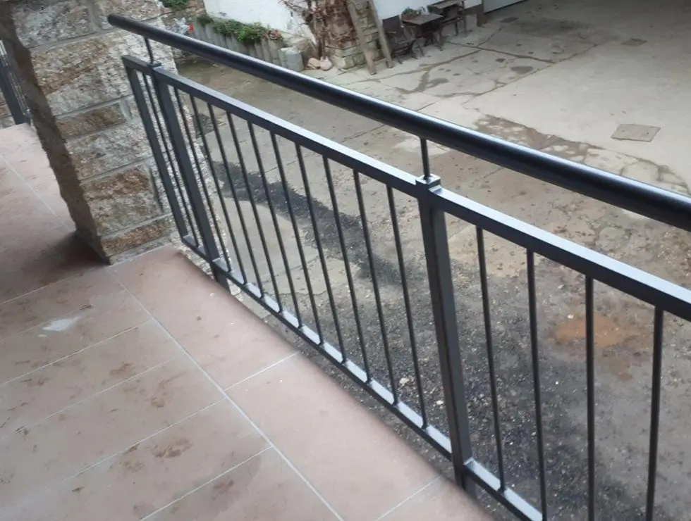 Metallgeländer mit senkrechten Stäben an einer Treppe vor einem gepflasterten Hof