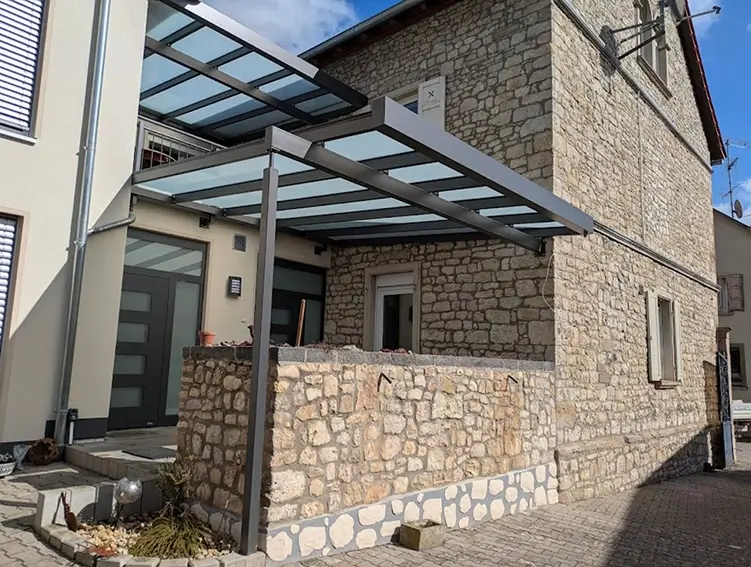 Haus mit Natursteinfassade und moderner Glasüberdachung über dem Eingang