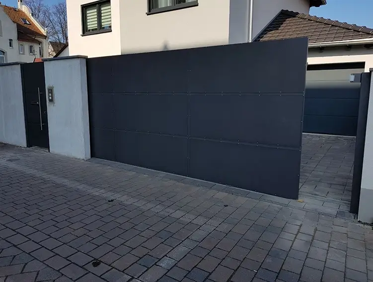 Schwarzes, modernes Schiebetor aus Metall vor einem Hof mit Häusern im Hintergrund
