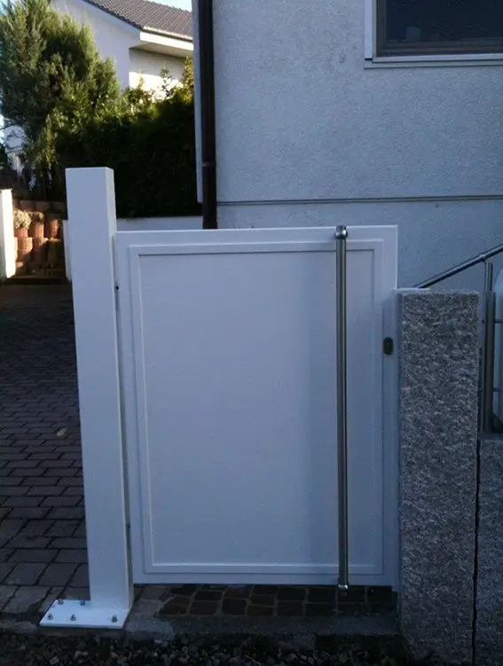 Weißes Gartentor mit Metallgriff zwischen weißem Pfosten und grauer Steinmauer