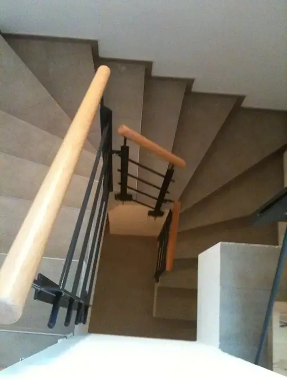 Blick von oben auf eine gewendelte Treppe mit Holzhandläufen und schwarzem Metallgeländer