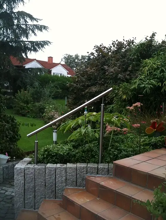 Edelstahlhandlauf an einer Treppe im Garten mit grünen Pflanzen und Häusern im Hintergrund