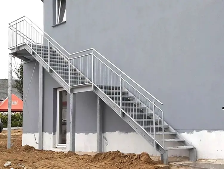 Außentreppe aus Metall mit Geländer an einem grauen Gebäude mit Fenstern