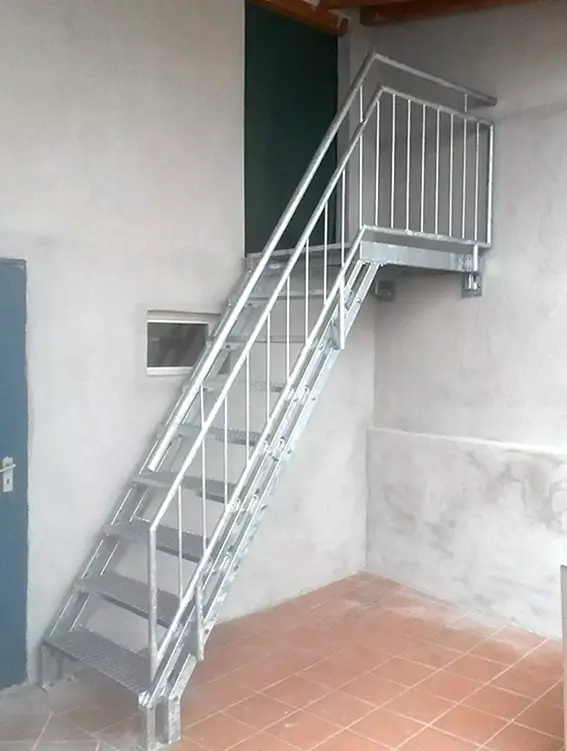Metalltreppe mit Geländer in einem Innenraum mit weißen Wänden und braunem Bodenbelag