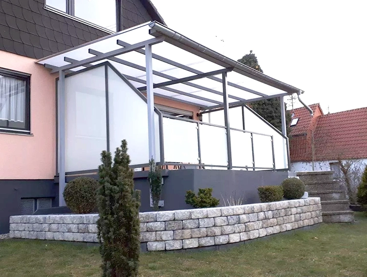Überdachte Terrasse mit Glasgeländer an einem Einfamilienhaus mit Steintreppe und Garten