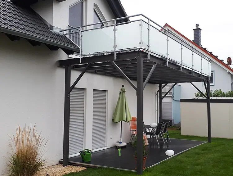 Moderner Balkon mit Glasgeländer an einem weißen Haus mit Terrasse und Garten