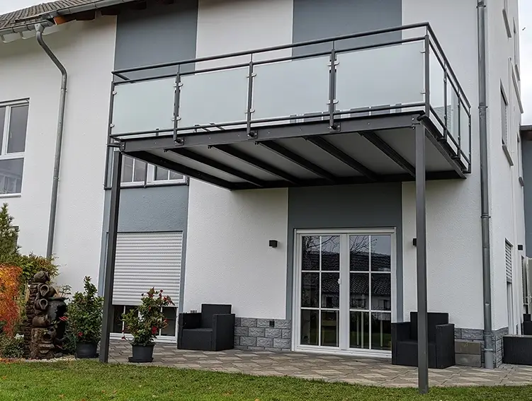 Moderner Balkon mit Glasgeländer an einem weißen Haus mit Terrasse und Garten