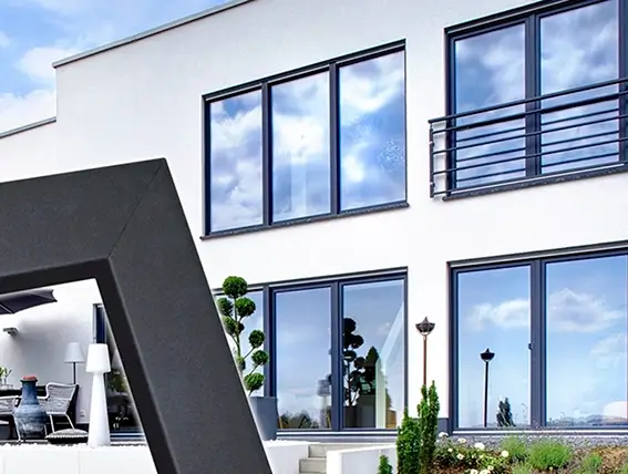 Moderner weißer Bau mit großen Fenstern und schwarzem Geländer vor blau bewölktem Himmel