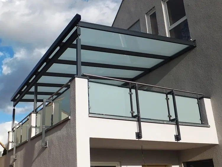 Moderner Balkon mit Glasgeländer an einem weißen Haus mit Terrasse und Garten