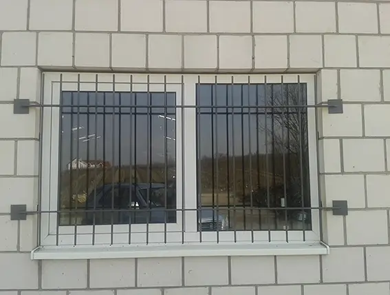 Fenster mit weißen Rahmen und schwarzem Gitter vor einer hellen Klinkerwand