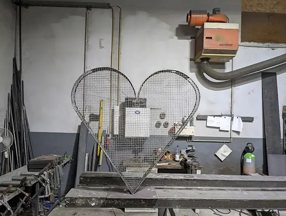 Herzförmiges Drahtgitter steht in einer Werkstatt vor einer Maschine