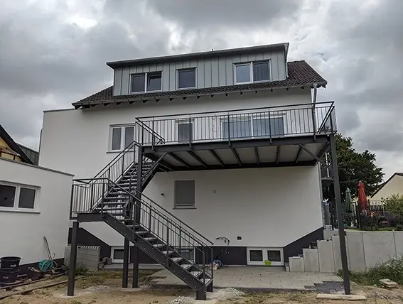 Haus mit aufgeständerter Terrasse und Außentreppe unter bewölktem Himmel