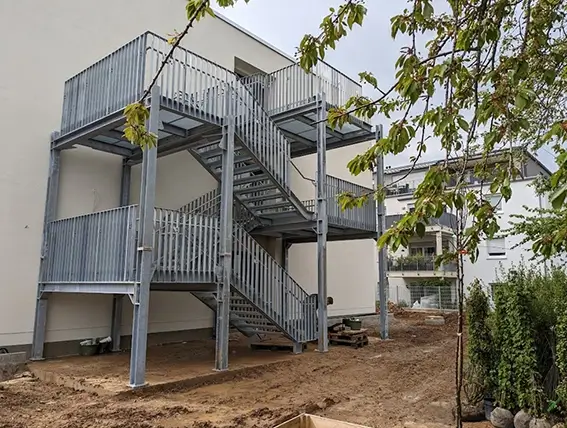 Außen liegende, mehrstöckige Metalltreppe an einem weißen Wohngebäude mit Geländer und Podesten