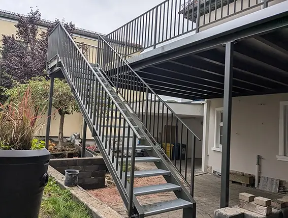 Außentreppe mit Metallgeländer führt zu einer erhöhten Terrasse an einem Haus