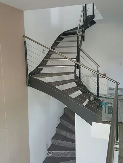 Geschwungene Treppe mit Metallgeländer und grauen Stufen in einem Innenraum