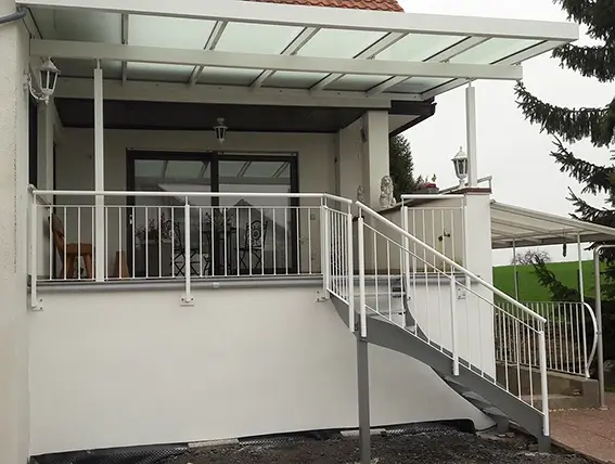 Außenansicht eines Hauses mit überdachter Terrasse und weißem Treppengeländer