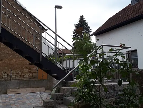 Außenbereich mit Steintreppe, Metallgeländer und Pflanzen vor einem Haus mit Fachwerkfassade