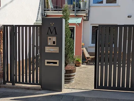 Eingangstor mit integriertem Briefkasten und Gegensprechanlage an einer Mauer mit Hausnummer und großem Buchstaben M