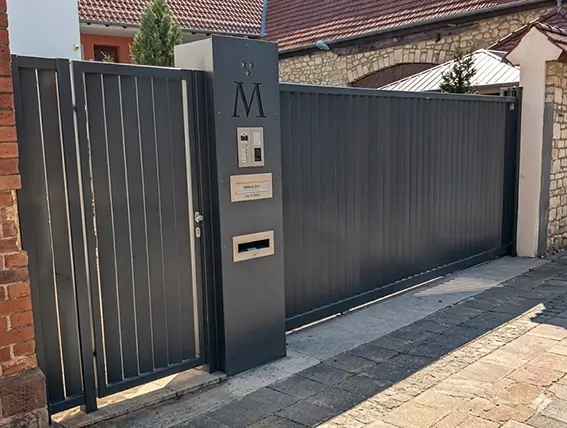 Eingangstor mit integriertem Briefkasten und Gegensprechanlage an einer Mauer mit Hausnummer und großem Buchstaben M