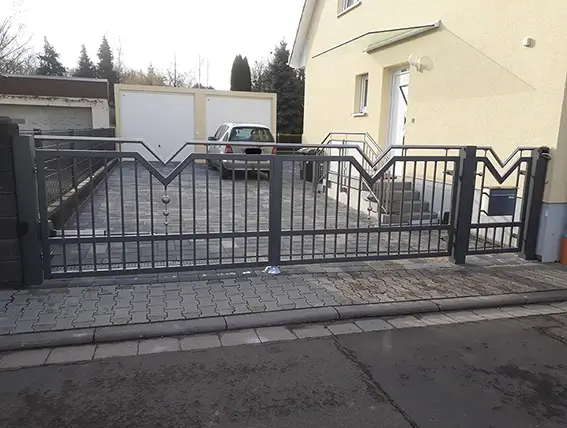 Einfahrt mit schwarzem Metalltor vor einem Haus und geparktem Auto