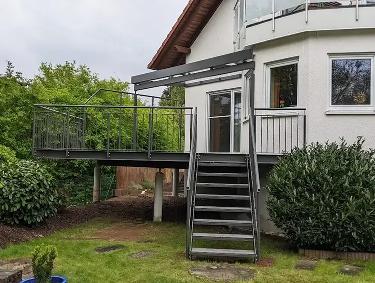 Haus mit einer erhöhten Terrasse aus Metall und einer Treppe, die zum Garten führt